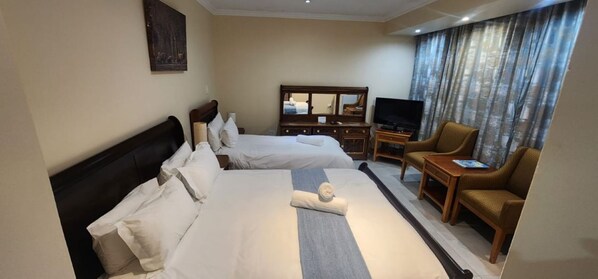 Habitación de hotel con dos camas, televisión, una silla y escritorio.