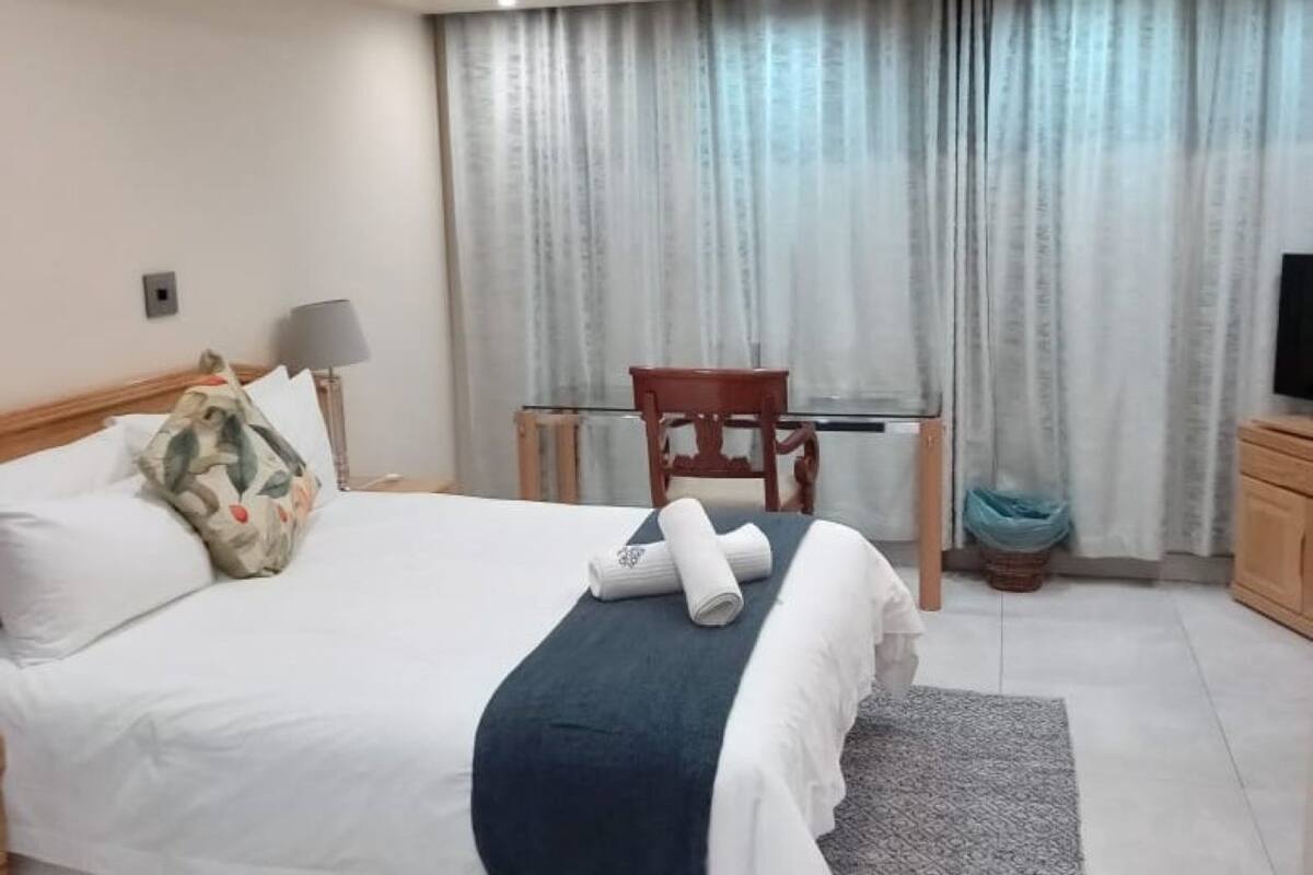 Una camera d'albergo con un letto, una sedia, una scrivania, una televisione e una finestra con tende.