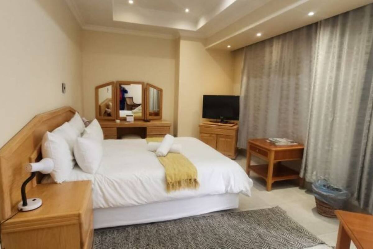 Una camera d'albergo con un letto, un comodino, una TV e una scrivania con una sedia.