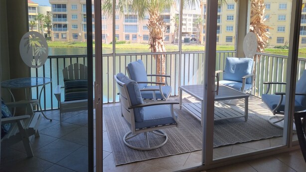 A balcony with two chairs and a table, overlooking a building and palm trees. - Luxury 3 Bed 2 Bath in FMB! Beach & Pool with the BEST reviews! (Fort Myers Beach)