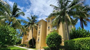 A yellow building with multiple balconies, surrounded by palm trees and well-maintained greenery. - Luxury 3 Bed 2 Bath in FMB! Beach & Pool with the BEST reviews! (Fort Myers Beach)