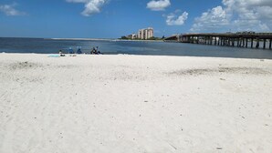 A beach with a pier extending into the water, a clear sky, and buildings in the distance. - Luxury 3 Bed 2 Bath in FMB! Beach & Pool with the BEST reviews! (Fort Myers Beach)