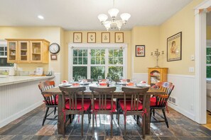 A dining area with a wooden table, red cushioned chairs, a chandelier, and framed pictures on the wall.