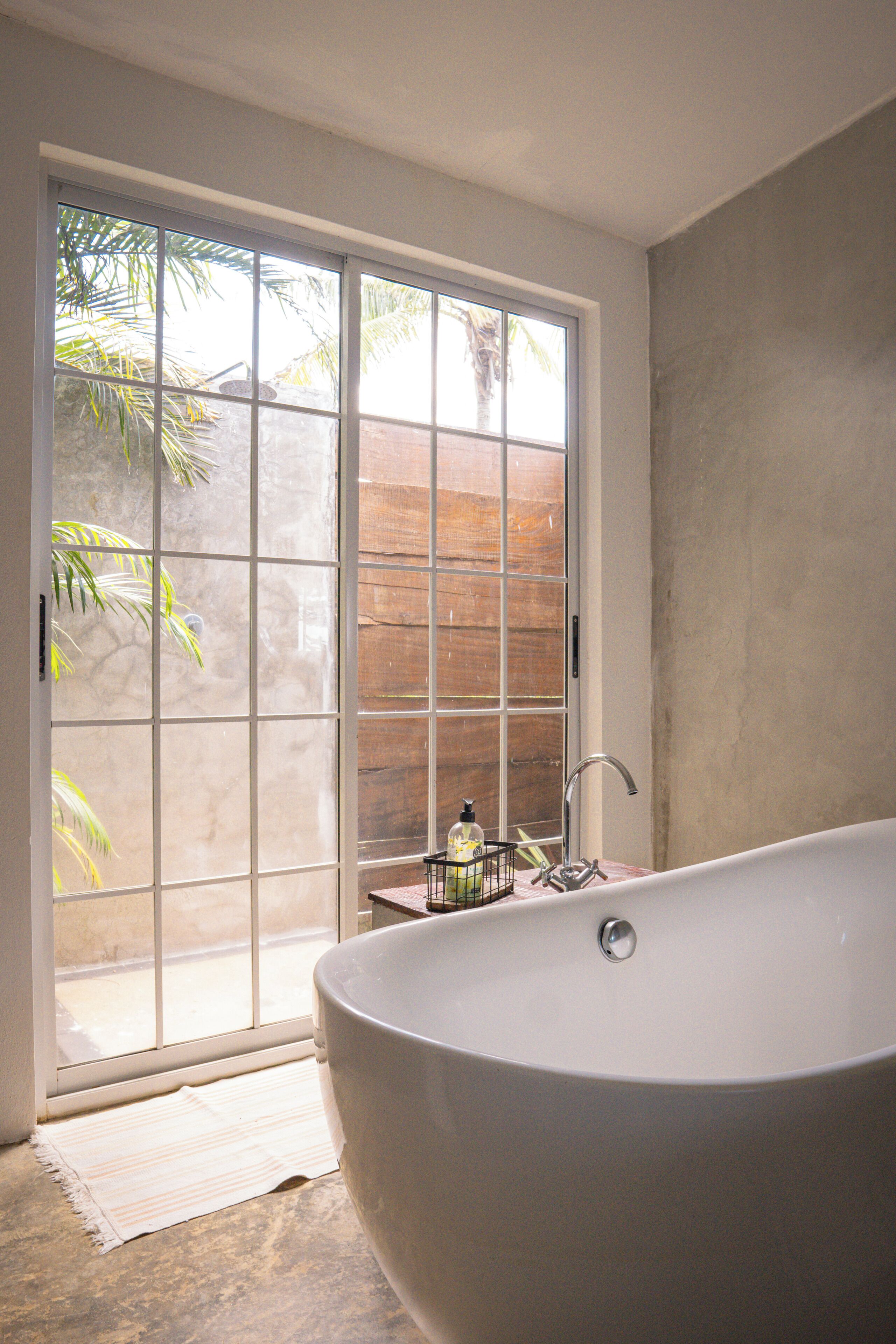 Ein Badezimmer mit einer großen Badewanne, einem Fenster mit Blick auf Palmen und einer kleinen Spüle.
