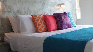 Un dormitorio con cabecera de hormigón, ropa de cama blanca y almohadas coloridas.