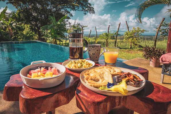 Una mesa de comedor con diversos platos, una jarrón y vasos de bebidas junto a una piscina.