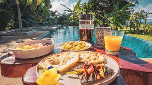 A breakfast setting by a pool with a plate of food, a pitcher of coffee, and a glass of orange juice. - La Maracuyá (San Jose)