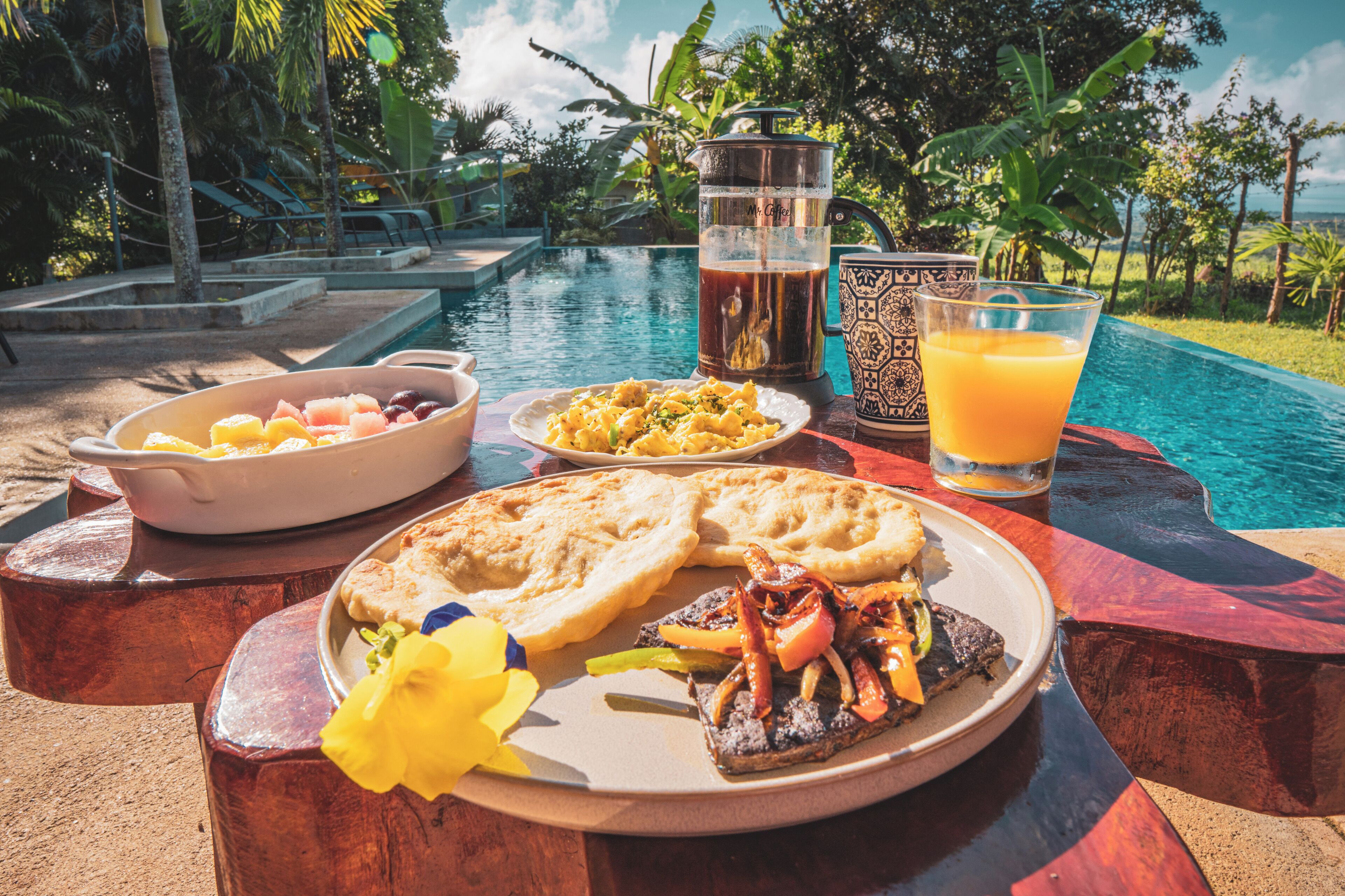 Desayuno junto a una piscina, con un plato de comida, una jarra de café y un vaso de jugo de naranja.