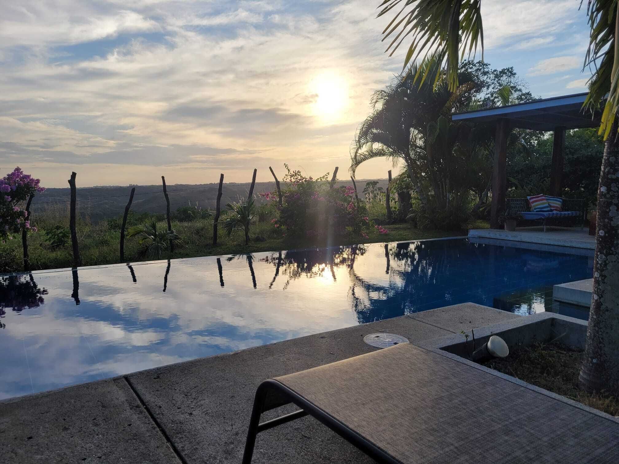 Una piscina infinita tranquila con una vista despejada del horizonte, rodeada de exuberante vegetación y una valla de madera.