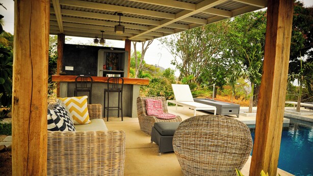 A covered outdoor seating area with wicker furniture, a bar, and a pool. - La Maracuyá (San Jose)