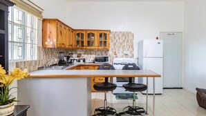 Une cuisine moderne avec des meubles en bois, un îlot central doté de tabourets, un réfrigérateur et un crédence carrelée.
