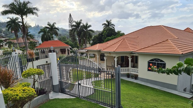 Un lotissement résidentiel fermé, doté d’une pelouse bien entretenue, d’une maison avec un toit recouvert de tuiles rouges et d ’une clôture blanche.