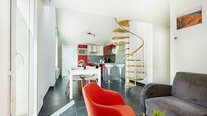 Een moderne woonkamer met een grijze bank, een rode fauteuil en een spiltrap.