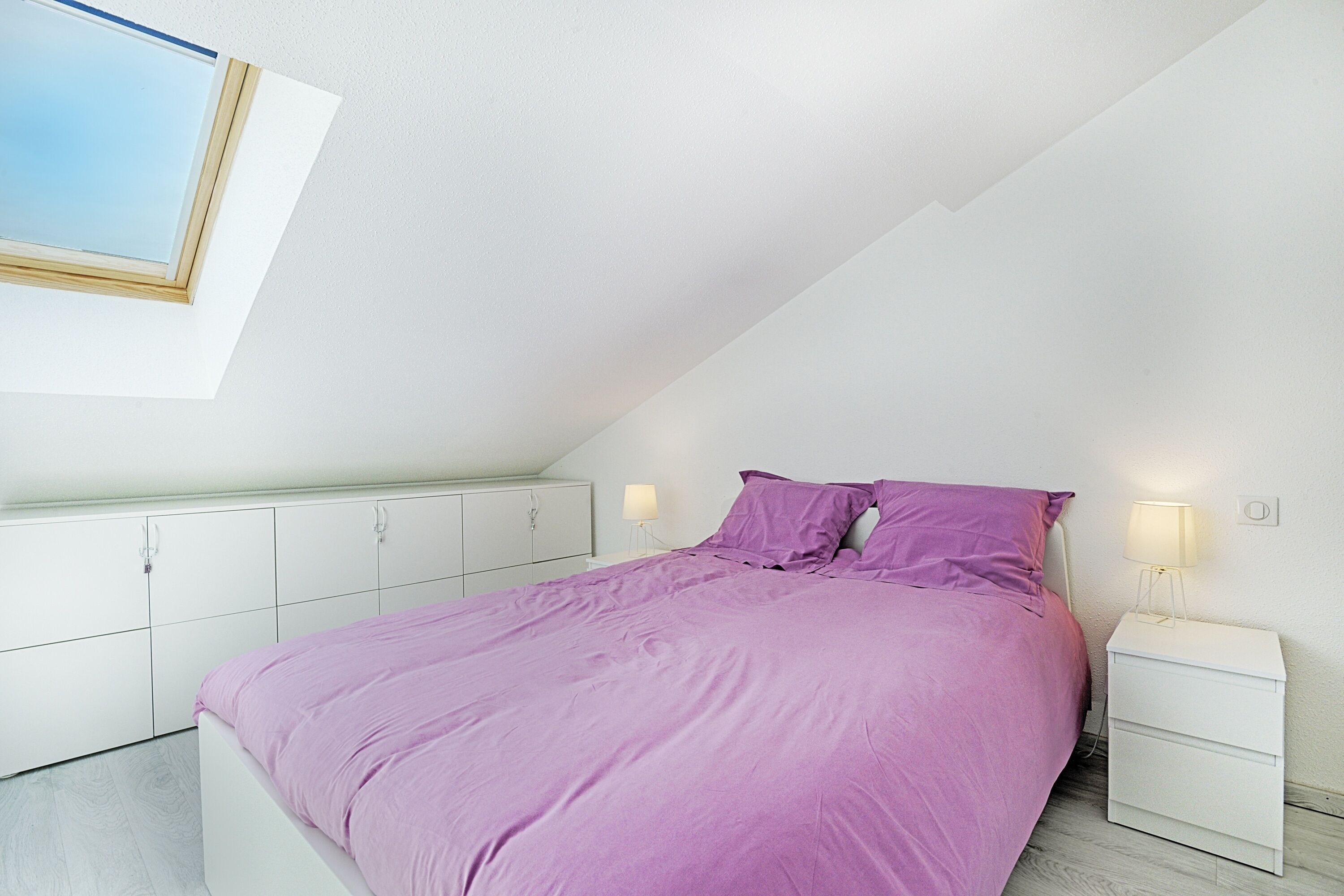 A bedroom with a bed, white cabinets, a nightstand, and a skylight.