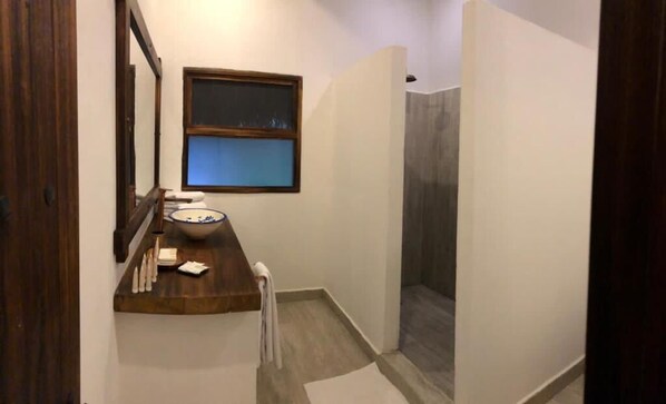 A bathroom with a wooden vanity, a mirror, a window, and a shower area.