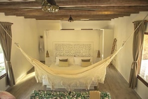 A bedroom with a large bed, a hammock, and a wooden ceiling.