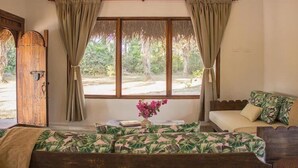 A room with a bed, a sofa, a window with curtains, a wooden door, and a vase with flowers. - Savanna Orinoquia Lodge (Orocue)