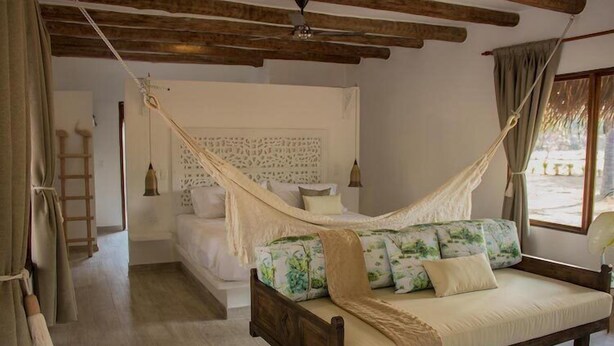 A bedroom with a wooden bed, a hammock, a ladder, and a view of the outside. - Savanna Orinoquia Lodge (Orocue)