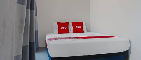 Una cama con dos almohadas, una manta roja y una colcha blanca.