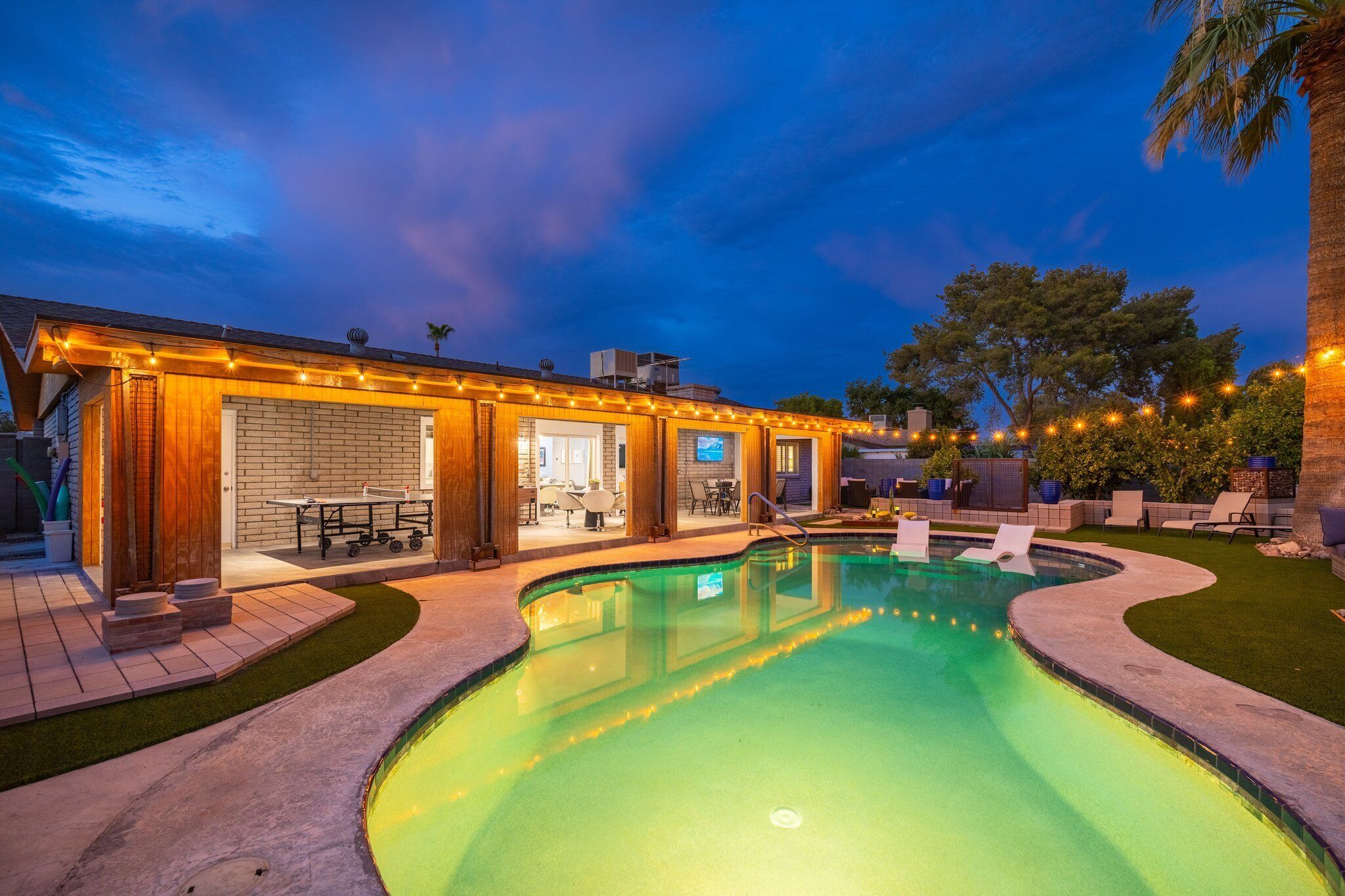 A swimming pool with a curved edge, surrounded by a patio area with outdoor furniture and string lights.