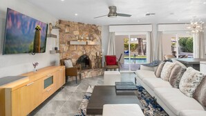 A modern living room with a stone fireplace, a sofa, a coffee table, and a TV mounted on the wall. - Luxury 4 Bed/4Bath! Private Pool & Mountain Views! (Phoenix)