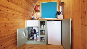 Eine kompakte Küche mit Holzwänden, einem Spülbecken, einem kleinen Kühlschrank und einem Regal mit Küchenutensilien.