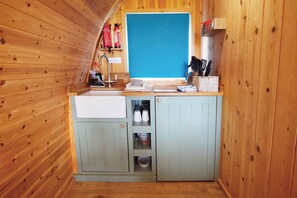 A compact kitchen with wooden walls, a sink, and cabinets containing kitchenware. - Ocean View 6 - 1 Bed Pod - Llanrhidian (Swansea)