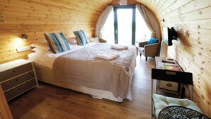 Ein gemütliches Schlafzimmer mit Holzbalkendecke, einem Bett mit beiger Bettdecke, einem Schreibtisch mit Laptop und einem Stuhl.