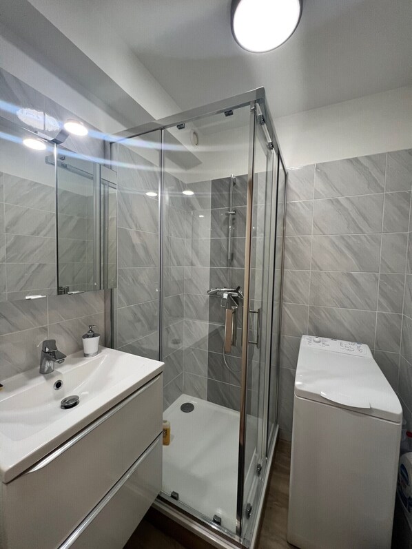 A modern bathroom with a glass-enclosed shower, a white sink, and a toilet. - vpark (Cannes)
