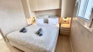 A bedroom with a bed, pillows, a nightstand, and a window.