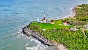 Un phare se dresse sur une falaise herbeuse, surplombant un rivage rocheux, une plage et offrant une vue dégagée sur l’océan.