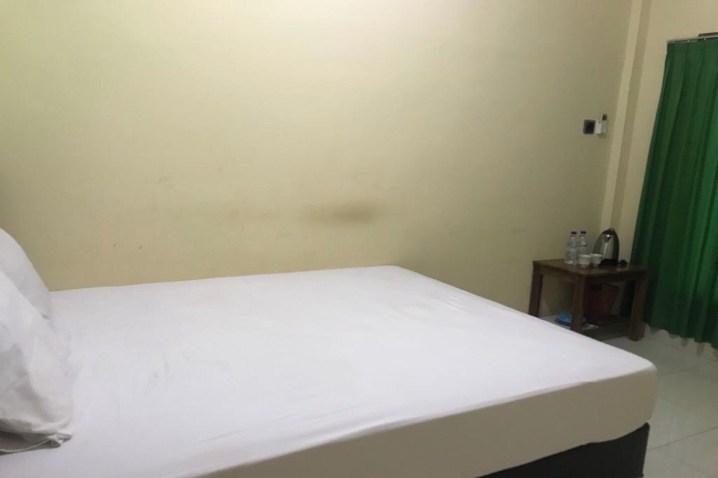 A simple room with a bed, a small table with toiletries, and a green curtain.