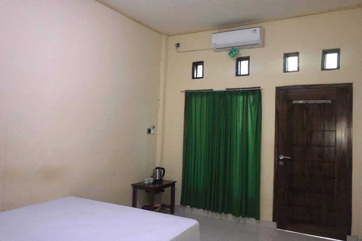 Una habitación con una cama, una mesita con una tetera, una cortina verde y una puerta de madera.