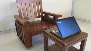 A wooden chair with a laptop on a small wooden table.