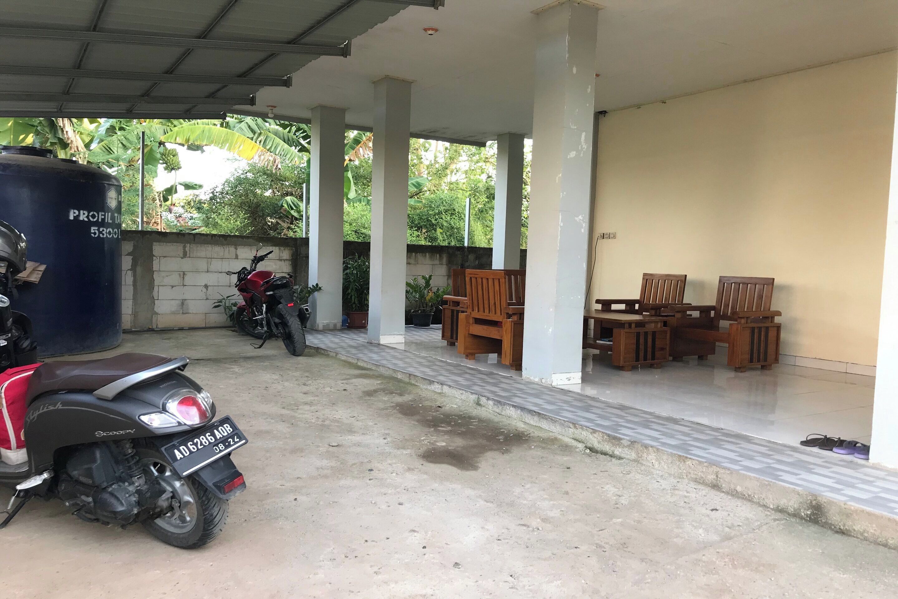 A covered outdoor area with a concrete floor, a water tank, and several wooden chairs and tables.