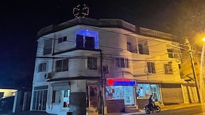 Un immeuble à plusieurs étages, avec une enseigne de pharmacie, un coin illuminé de lumière bleue et une moto garée devant.