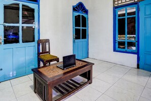 A room with a wooden table, a chair, and a laptop. There are blue doors and a window with a curtain. - Hotel O Umi Homestay Syariah (Sidoarjo)