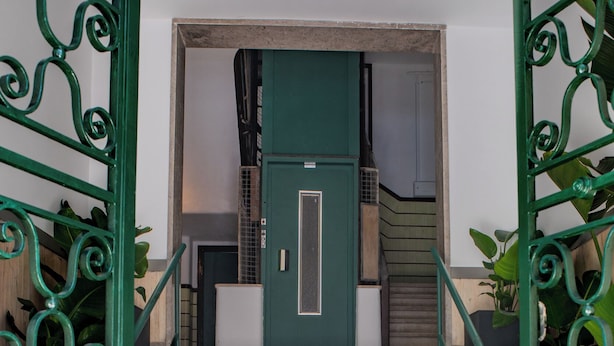 A staircase with green metal railings leading to a room with a green door and a white cabinet.