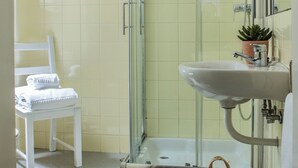A bathroom with a glass-enclosed shower, a white sink, and a chair.