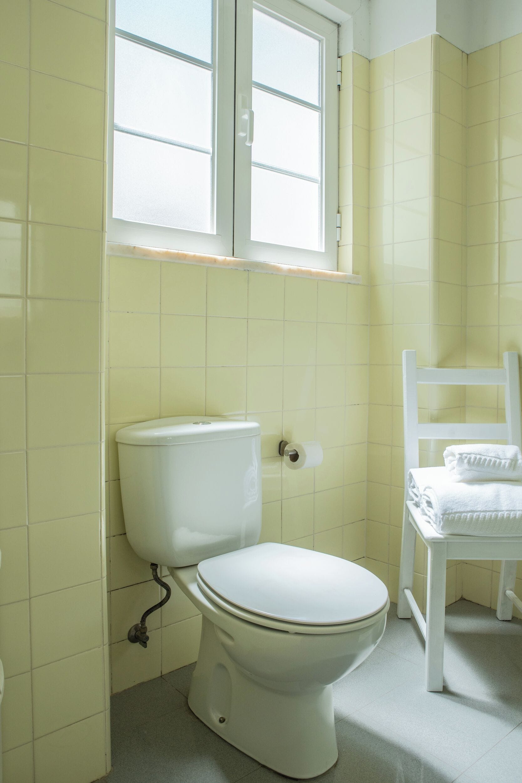 Une salle de bain avec des toilettes, une fenêtre et une chaise.