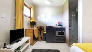 A compact kitchen with a microwave, oven, and sink, a small dining area with a TV, and a shower area. - Ocean View 7 - 1 Bedroom - Llanrhidian (Swansea)