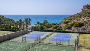 A tennis court with a view of the sea and a rocky hillside.