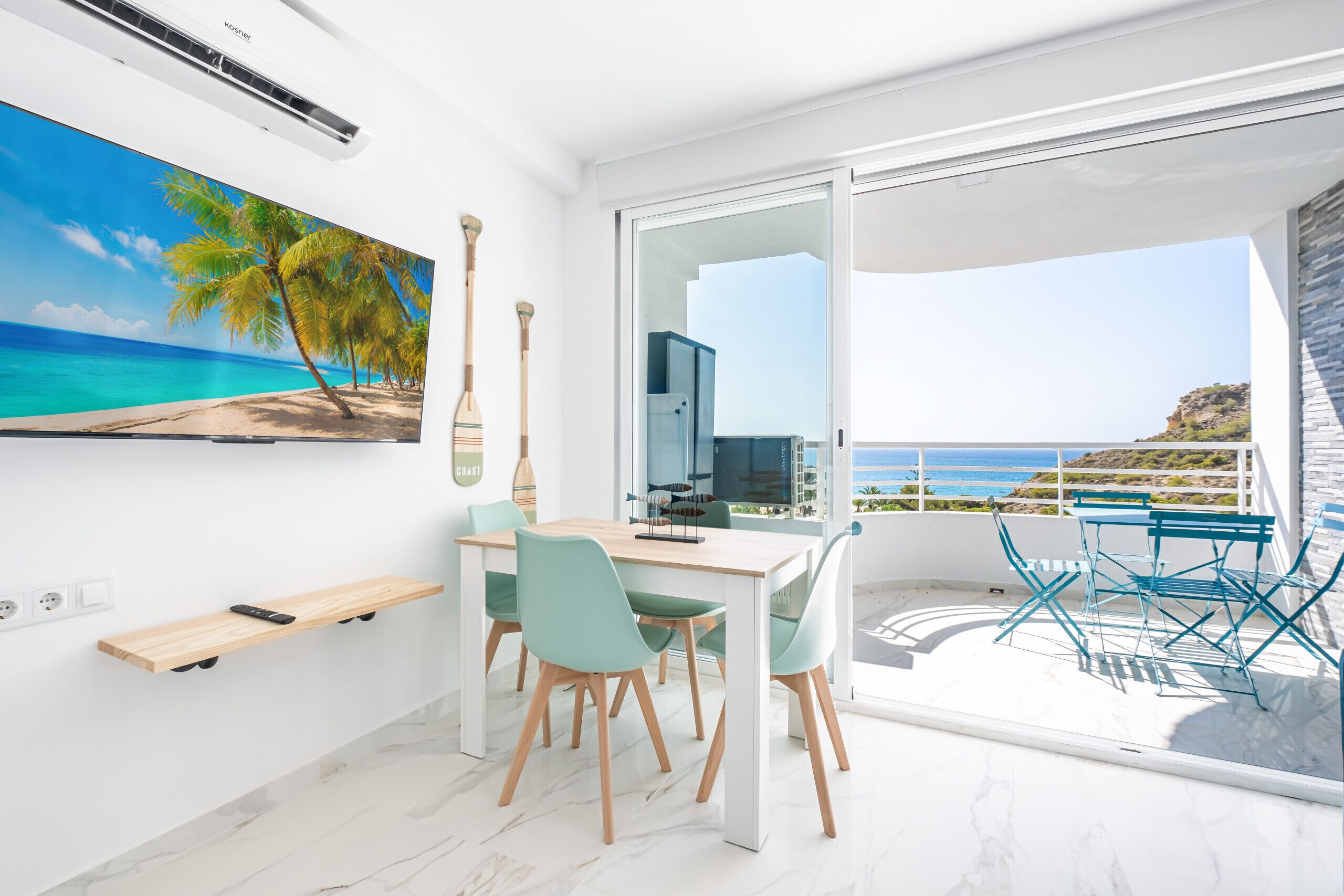 Une chambre moderne avec un coin repas, une grande fenêtre donnant sur la mer et un tableau représentant une scène de plage.