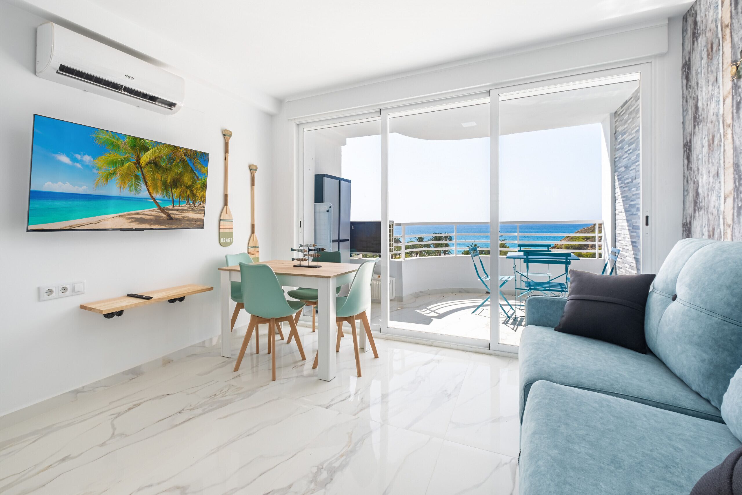 Uma sala de estar moderna com uma televisão grande, uma área de refeições e uma varanda com vista para o mar.