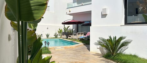 A modern house with a swimming pool, outdoor seating, and lush greenery.