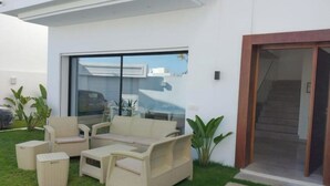 A modern outdoor seating area with a sofa and chairs, a small table, and a trash bin. - Villa a Hammamet Centre, 300 Metre du Theatre, Piscine, Climatisée, 4 Chambre (Hammamet)