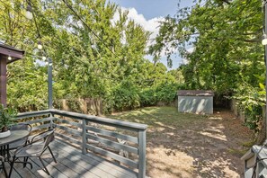A covered patio with a table and chairs, surrounded by trees and a wooden fence.