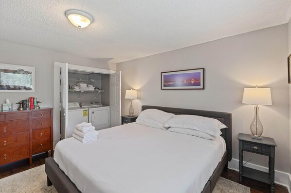A neatly arranged hotel room with a bed, bedside lamps, a wardrobe, and a closet with folded towels.