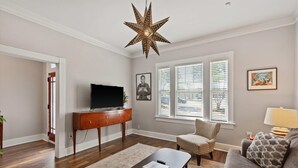 Ein Wohnzimmer mit einer sternförmigen Leuchte, einem Fernseher auf einem Holzboden, einem Sofa und einem gemusterten Teppich.
