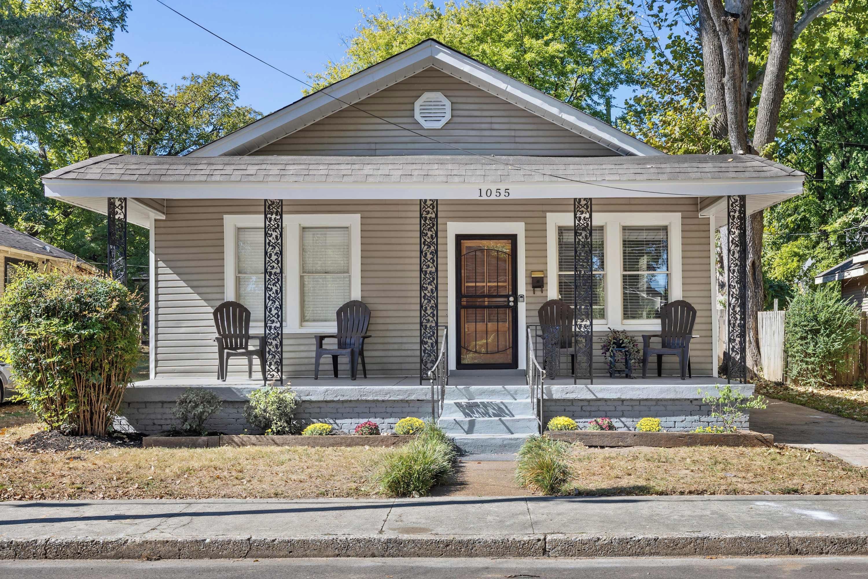 A single-story house with a gabled roof, a front porch with two chairs, and a small garden area.